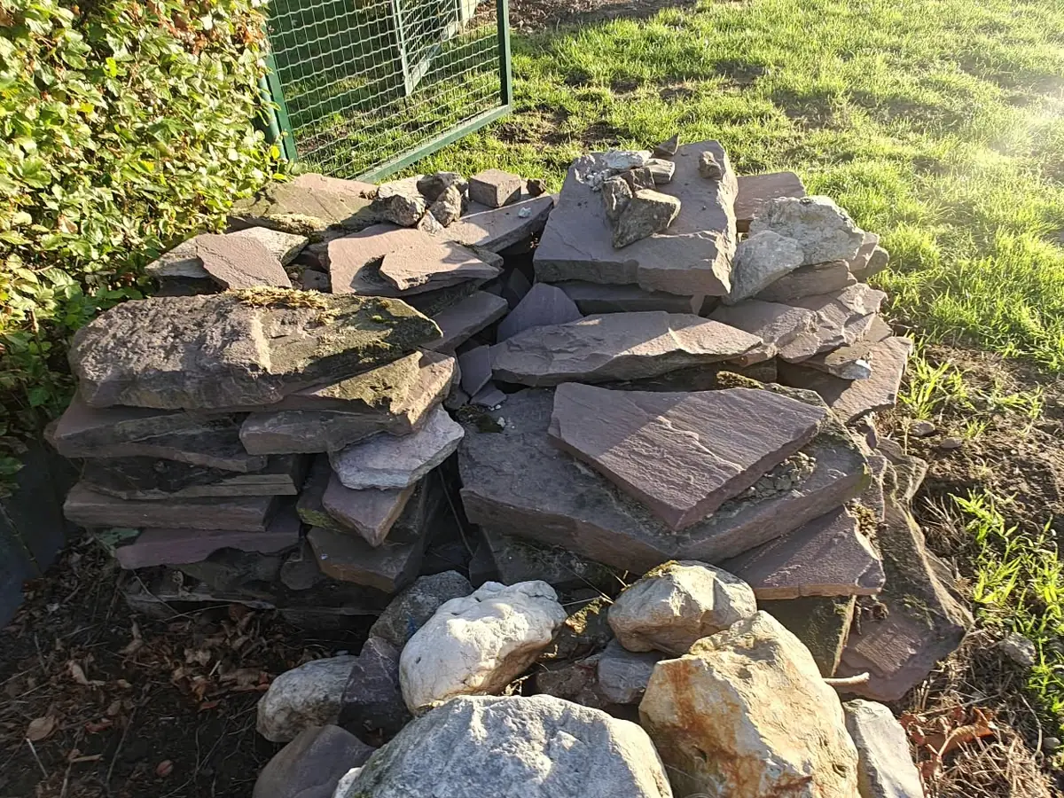 Stapel natuurstenen platen en rotsblokken in een tuinhoek voor de opruiming