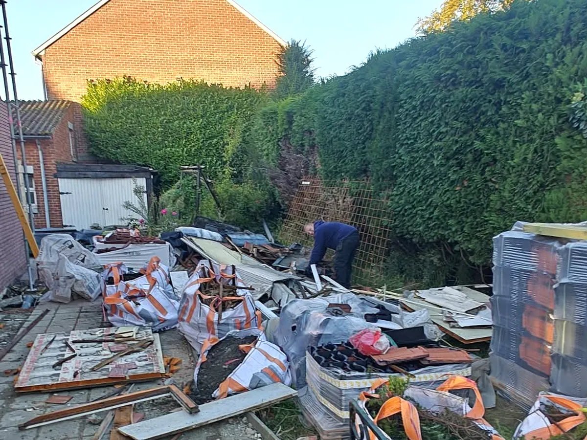 Tuinpad en berm vol gebroken dakpannen, planken en sloopafval voor de opruiming door JG Services in Limburg